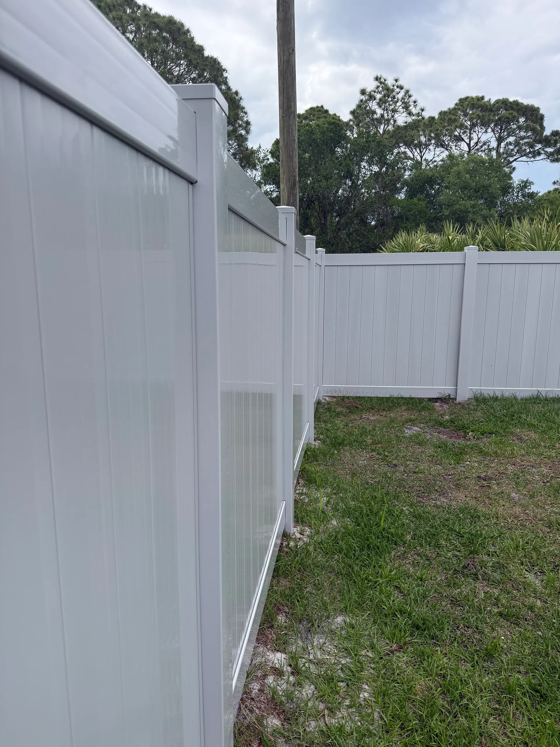 White vinyl privacy fence perspective view alongside a freshly seeded yard